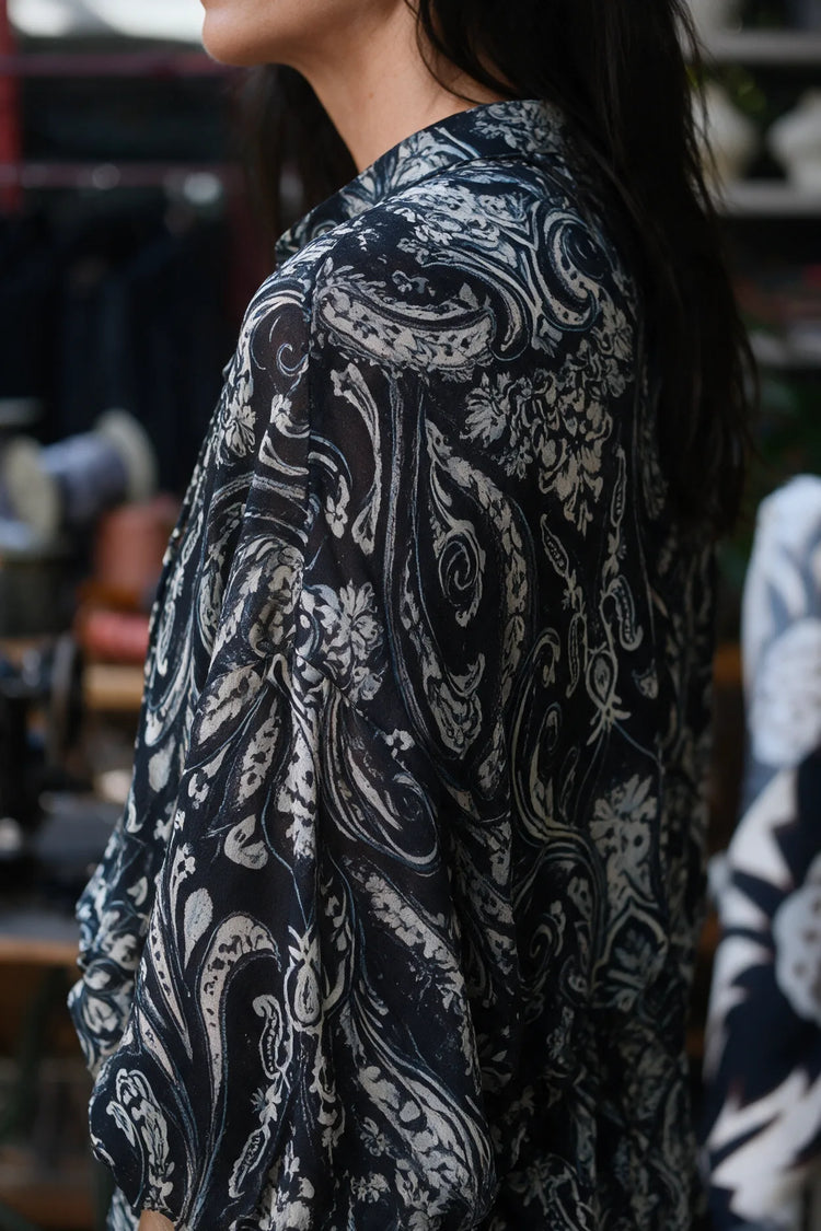 Blusa romántica negra de gasa con estampado paisley crudo, detalle lateral y trasero.