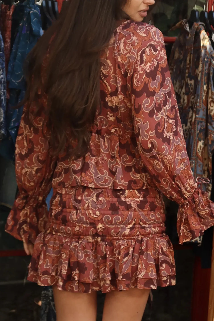 
                  
                    Blusa de gasa con estampado paisley terracota, escote en V con volante y mangas amplias, vista de tres cuartos.
                  
                