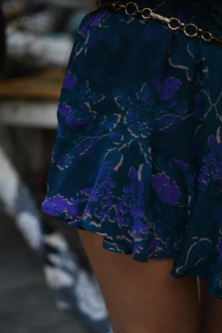 Short de gasa con estampado floral violeta sobre fondo turquesa y ruedo con vuelo, detalle del ruedo con vuelo.
